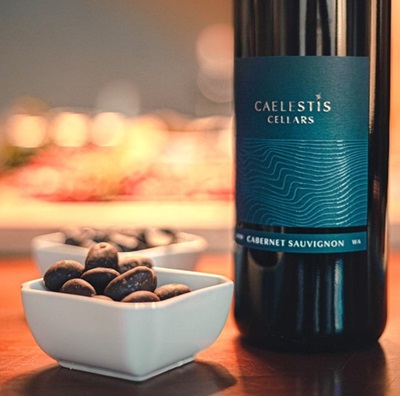 A bottle of wine next to a bowl of snacks