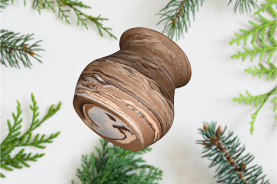 A marbled ceramic vase in front of pine tree branches on a white background.