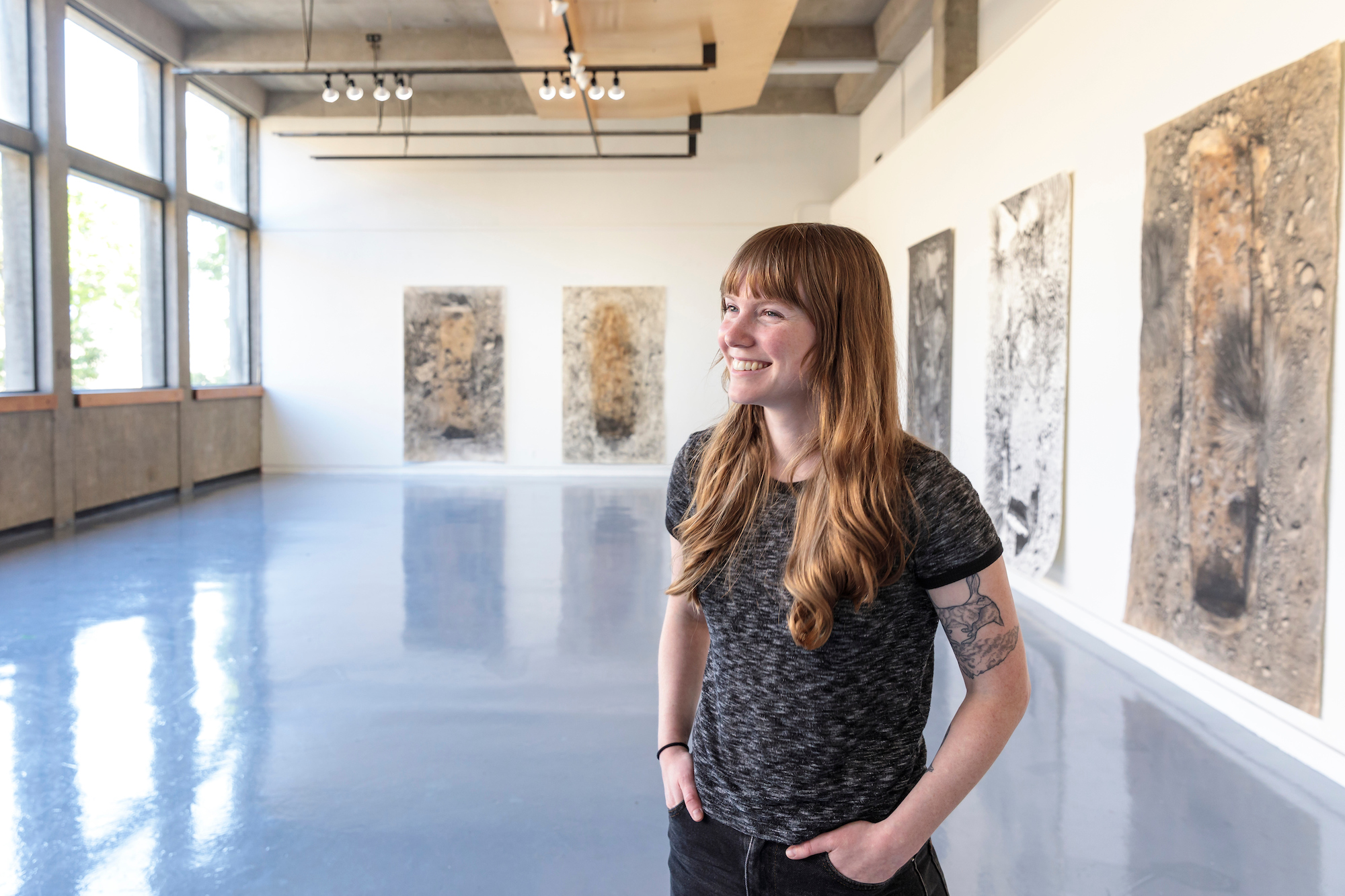 Graduate student standing in gallery with her graduate project exhibition in background