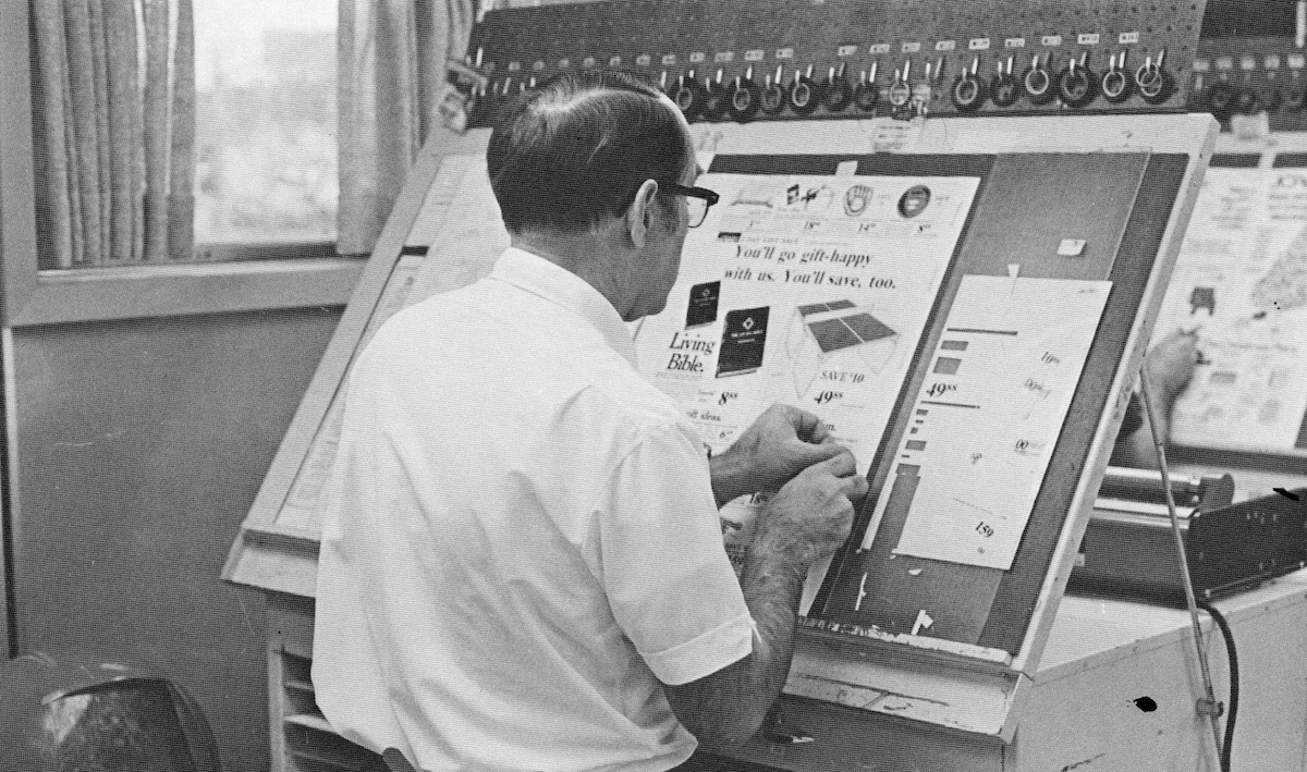 Man working at a drafting table working on paste up board for an ad