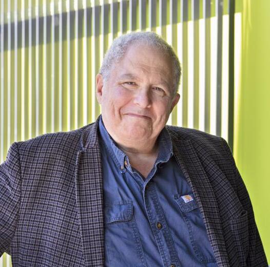 Robert Strongin, a white man with grey hair smiling at the camera in front of a green background. 