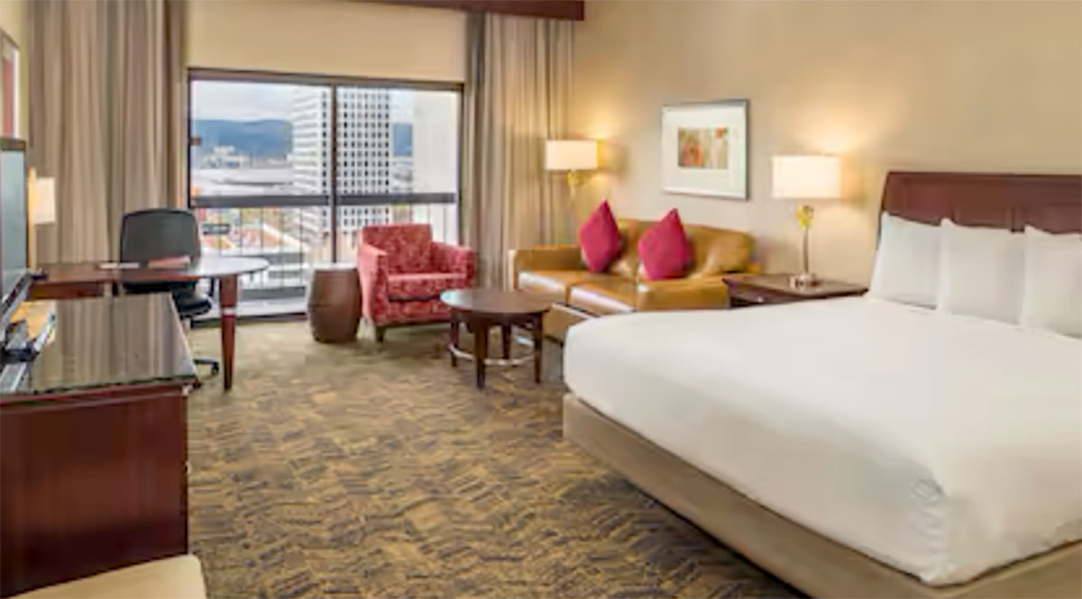 A king-sized bed, seating and desk with a view of the Lloyd District in a room at the Doubletree Hilton in Portland.