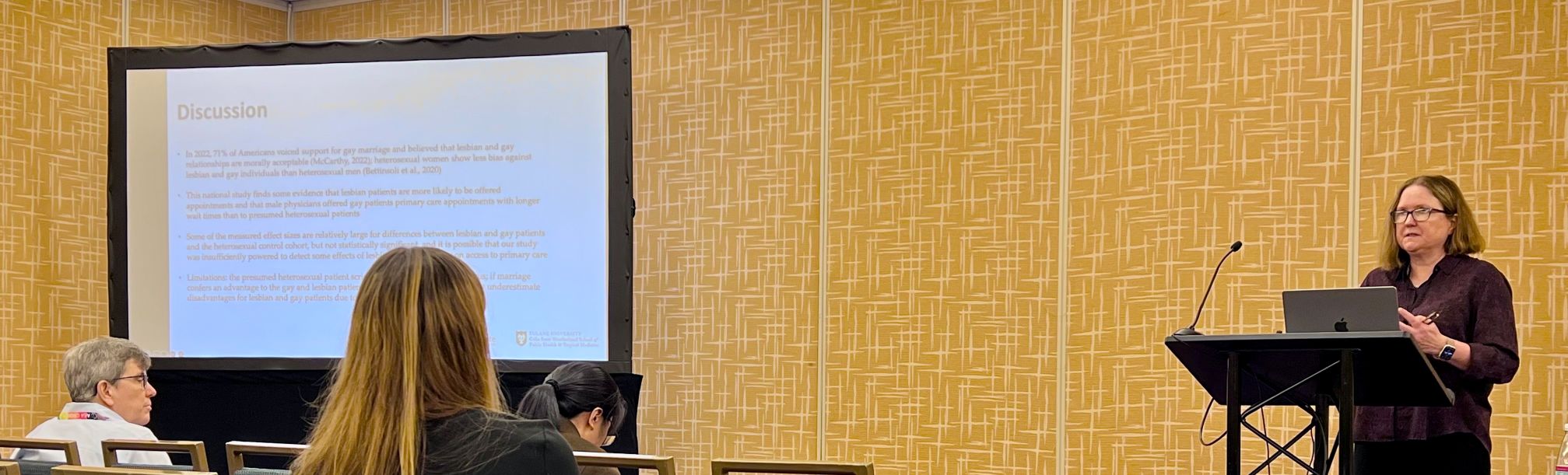 Sarah Tinkler at a podium presenting paper with PowerPoint slide to her right