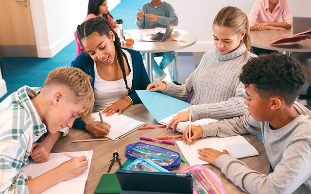 A group of teenagers are gathered together working on schoolwork.
