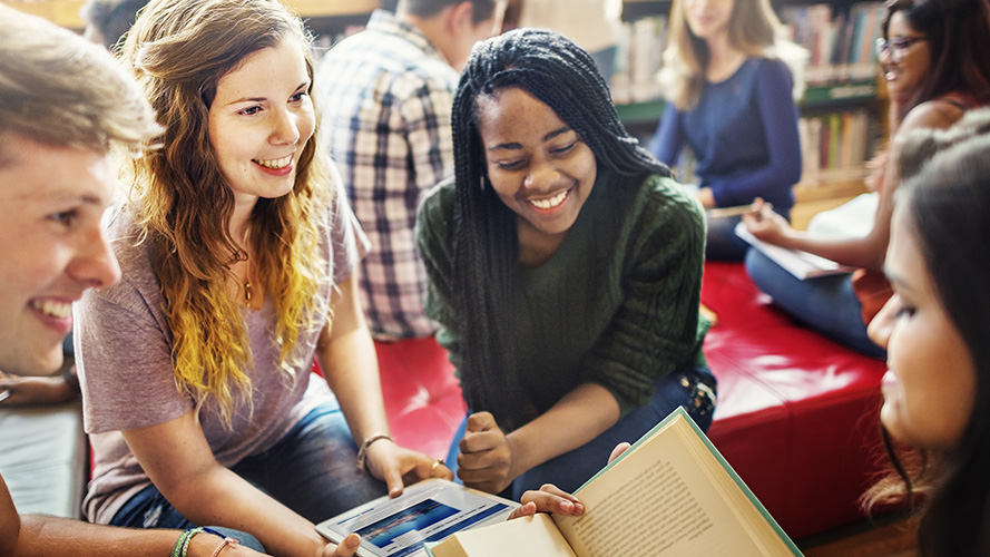 A grouop of smiling high school students are gathered in a library.