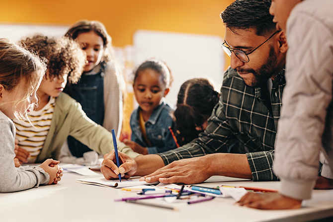 A teacher in a plaid shirt and glasses shows students how to complete an assignment.