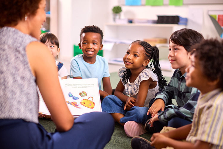 A group of grade school children sit around their teacher on the floor for story time.