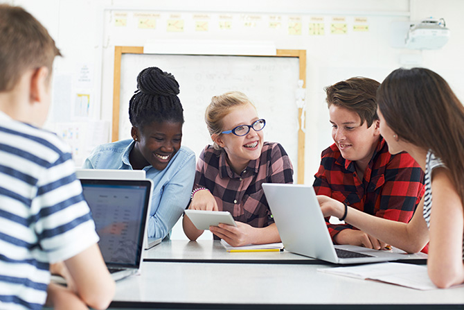 A group of teenagers are gathered together on laptops and tablets.
