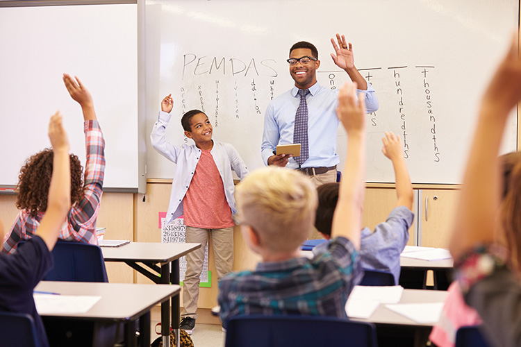 A teacher stands at the front of a math class teaching the order of operations.