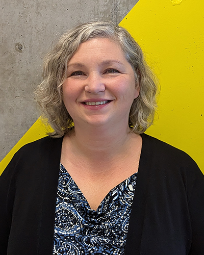 Tatiana Nochevnaya, Admissions Advisor. A Russian woman with a curly silver-blonde bob and a bright smile. She wears a navy paisley shirt under a black cardigan.