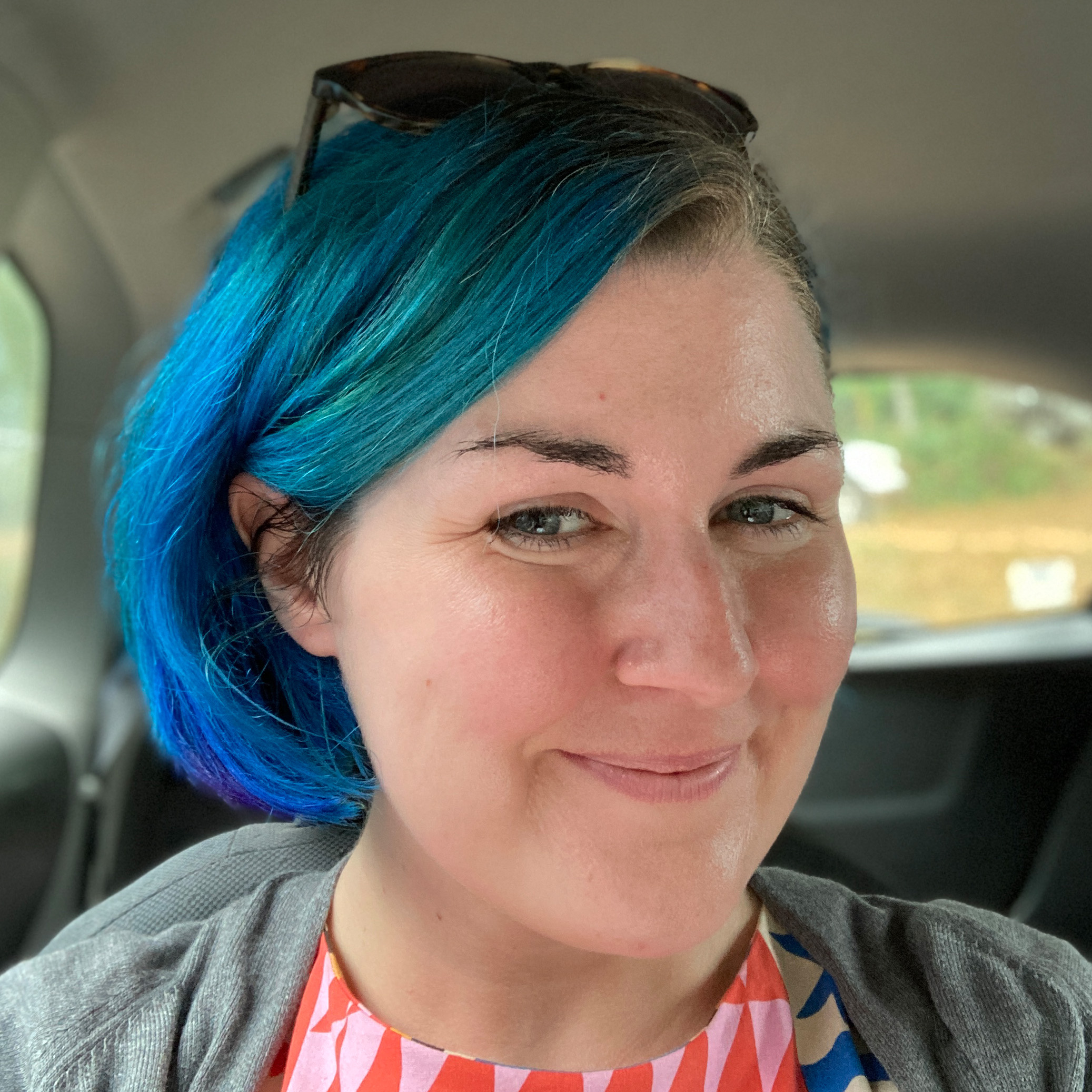 Picture of person with short blue hair and sunglasses on the top of their head