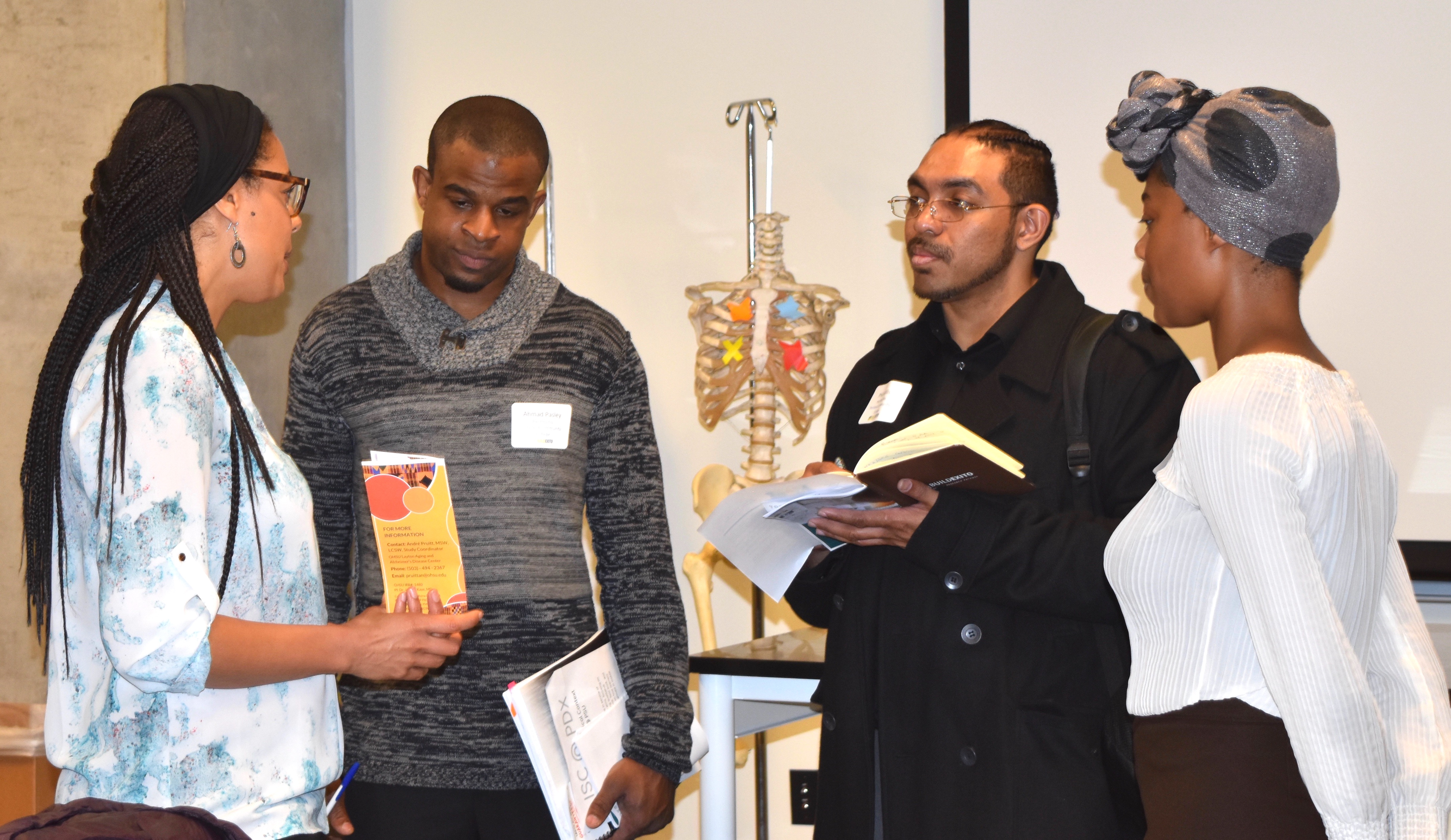 3 students stand and listen to a faculty talk about their lab