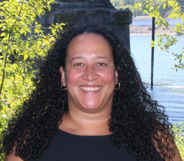 Photo of Shannon Singleton standing in front of a body of water and some trees. 