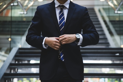 Photo by Hunters Race, from Unsplash.com. Image of a man buttoning a business suit on a set of stairs