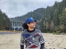 Person standing on beach in front of a bridge