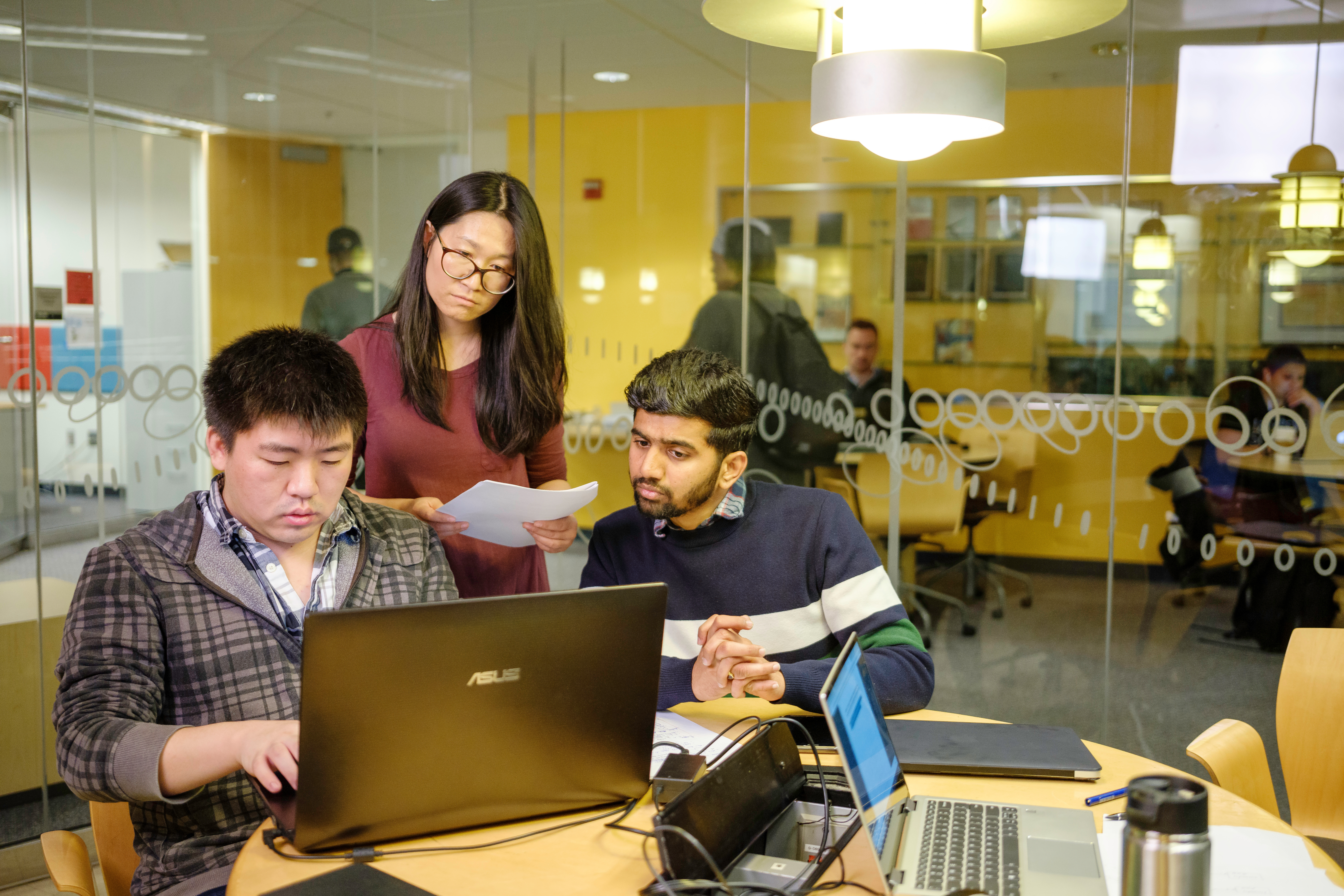 Three students around a table looking at a laptop. One student appears to be typing